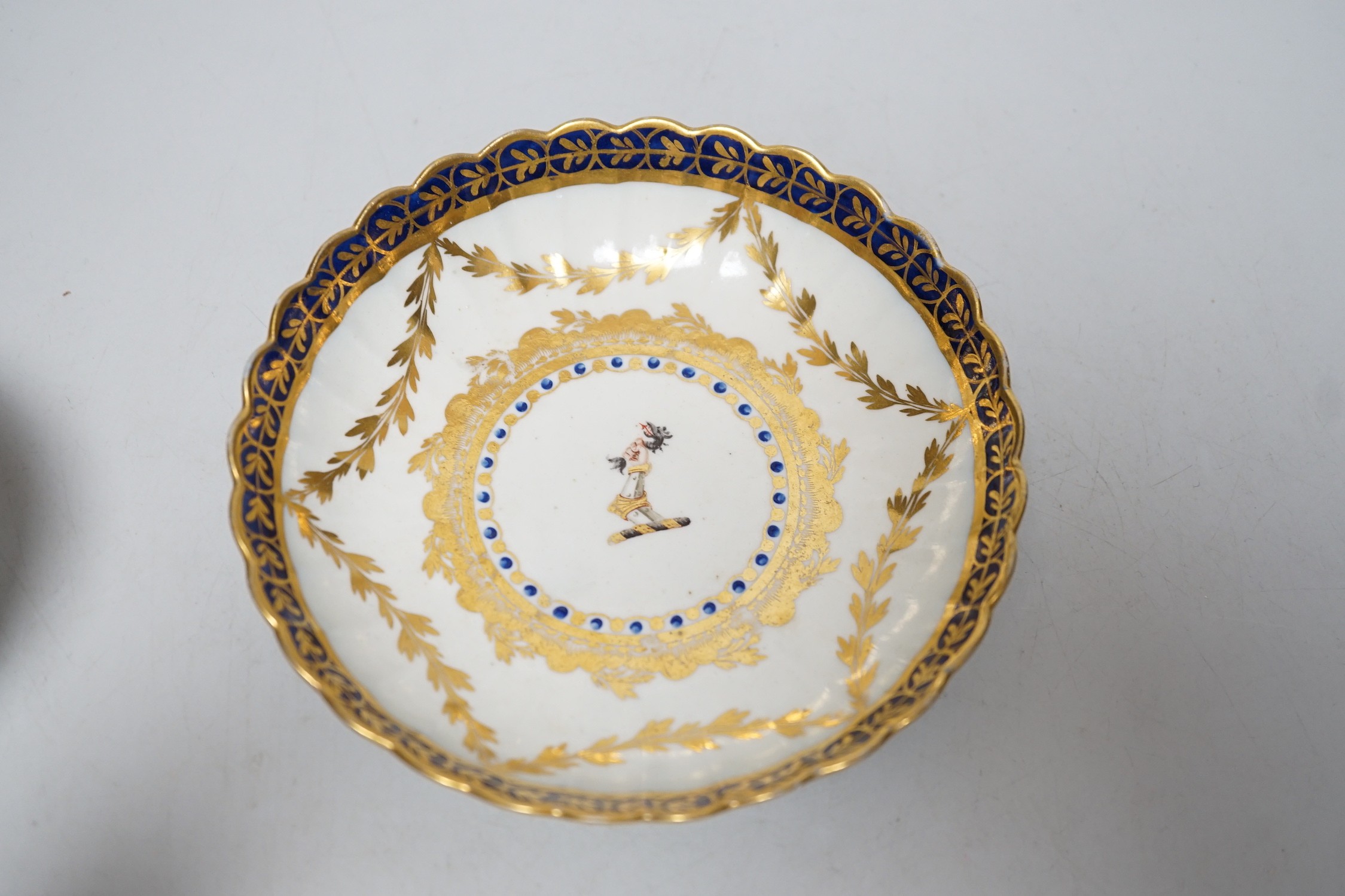 An 18th century Caughley rare teabowl and saucer painted with a crest of an arm clutching a dragon encircled by three gilt borders, 6cm tall overall